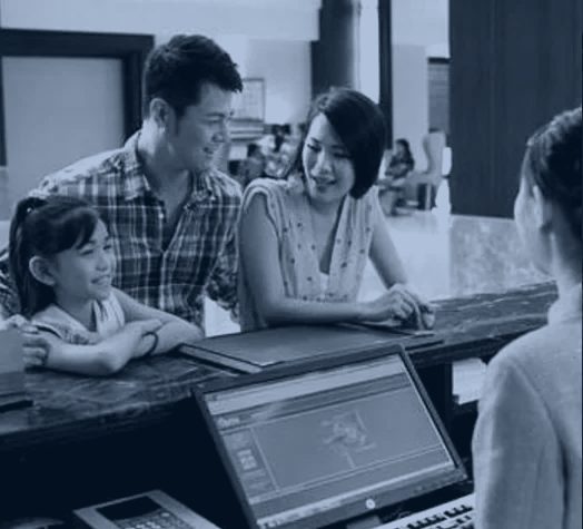 Recepción de un hotel: personal atendiendo a una familia con el sistema de gestión en pantalla.